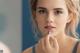 A woman putting lipstick on her lips in front of a mirror.