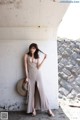 A woman leaning against a wall with a straw hat.